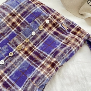 Détails des boutons décoratifs et de l'étiquette sur la chemise à carreaux violets