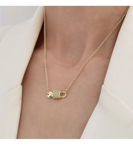 Detailansicht eines Modells mit goldener Halskette und funkelndem, diamantbesetztem Schlossanhänger