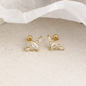 Gros plan de boucles d'oreilles dorées en forme de feuille avec zircons sur tissu beige doux