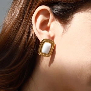 Close-up of elegant gold-rimmed rectangular stud earrings with white inlay on ear