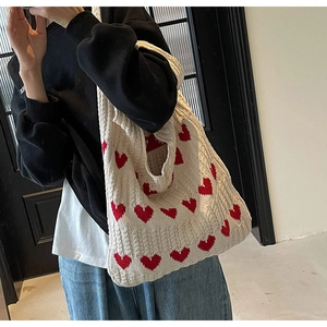 Primer plano de un bolso tote de punto crema con corazones rojos al hombro