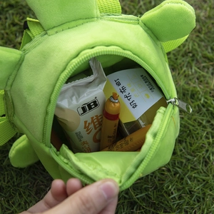 Green dinosaur plush backpack for small dogs and cats with snacks inside on grass