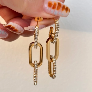 Detailed view of hand-held gold long chain earrings with sparkling white zircon stones