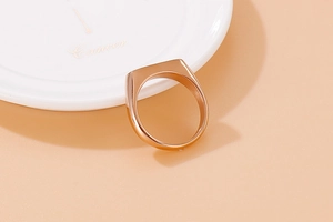 Detailed view of a polished rose gold signet ring on a white porcelain tray