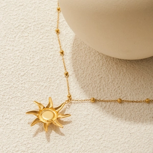 Nahaufnahme einer goldenen Sonnenanhänger-Halskette mit Perlenkette auf Textur
