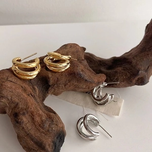 Dettaglio di orecchini a cerchio ovali color oro e argento su legno rustico e stoffa
