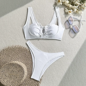 Flat lay of white cutout bikini set with sunglasses and straw hat on woven mat