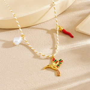 Detail of woven rope necklace featuring gold hummingbird, red chili, and pearl pendants