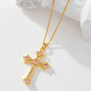 Detailed view of a gold cross pendant with pink gemstones on a white textured background
