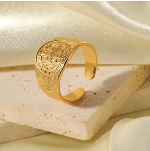Detail of 18K gold-plated Saint Benedict medal ring on beige travertine with silk