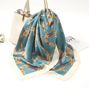 Detail of teal silk scarf with gold chain print draped elegantly over a white handbag