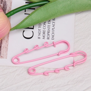 Detail of two pink 6cm lacquered safety pins with curly loops on white fabric