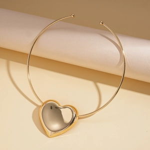 Detailansicht eines glänzenden goldenen Herzanhängers am Choker auf beigem Sockel