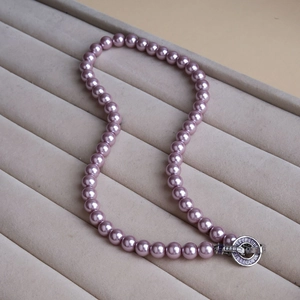 Macro detail of lavender pearl necklace with gemstone buckle on a gray velvet display