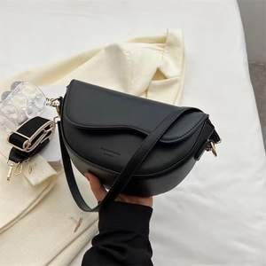 Close-up of black leather saddle bag with gold metal buckle and wide jacquard strap