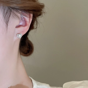 Macro shot of silver heart stud earrings with sparkling stones on a model ear