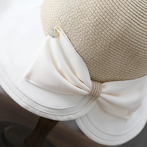Macro detail of French straw sun hat featuring a white ribbon bow and gold metal crest