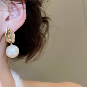 Close-up of pearl earrings with golden hammered metal studs on a model's ear