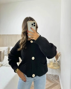 Détail d'un cardigan noir à grosse maille avec de gros boutons dorés et des poches carrées