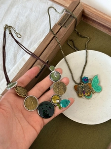 Detailed view of bronze butterfly pendant and retro multi-disc necklace on wood