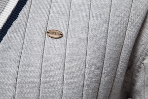 Dettaglio del cardigan grigio a coste con scollo a V e logo metallico del brand