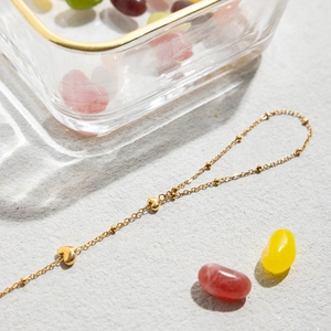 Detailed close-up of 18K gold stainless steel heart pendant bracelet on stone surface