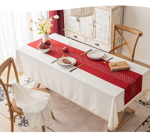 Close-up of cream tablecloth with red table runner and intricate hollow-out lace patterns