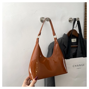 Detail of glossy brown patent leather hobo bag with gold buckle on shoulder strap