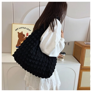 Close-up of black puffer tote bag with quilted texture worn on model's shoulder
