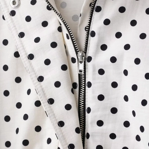Dettaglio del tessuto a pois bianchi della giacca con zip metallica e trama intrecciata