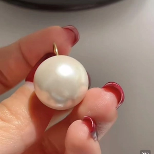 Close-up of a high-luster white pearl earring with a 14K gold plated clasp held by hand