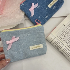 Dettaglio di portamonete in denim con trama a cuore, fiocchi rosa e zip gialle a contrasto
