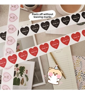 Macro view of heart-shaped Thank You stickers in red and pink on a warm desk background