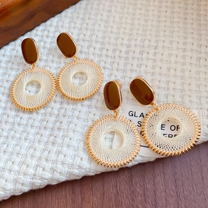Detail of bohemian round woven hoop earrings with champagne thread on white fabric