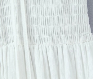 Detail shot of the white pleated fabric texture and delicate tie straps on the dress