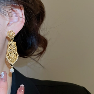 Detail of vintage gold hollow long earrings with elegant pearl drop on a model