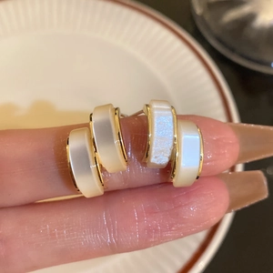 Close-up of mother-of-pearl stud earrings with gold trim held between fingers