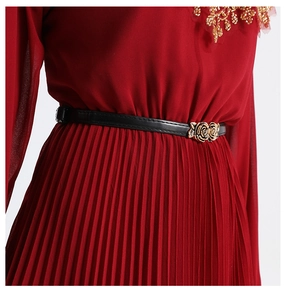 Detailed view of red pleated chiffon dress with gold sequins and black rose buckle belt
