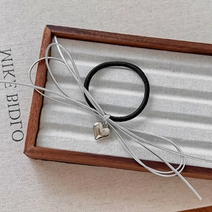 Close-up of hair tie set with silver heart pendant and ribbon in a wooden tray