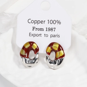 Detail of red and gold enamel earrings in a white ceramic dish with copper material tag