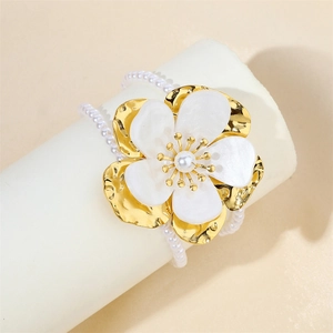 Macro detail of 18k gold-plated floral charm with shell inlay and pearl chain bracelet