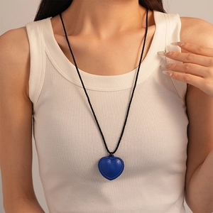 Gros plan du pendentif cœur bleu foncé avec bordure tissée sur cordon noir porté par modèle