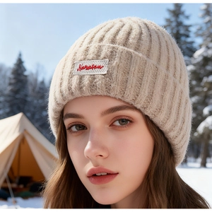 Dettaglio del berretto in maglia beige con trama a coste spesse ed etichetta sulla neve