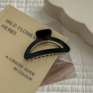 French minimalist black arched hair claw with gold metal teeth on a vintage book