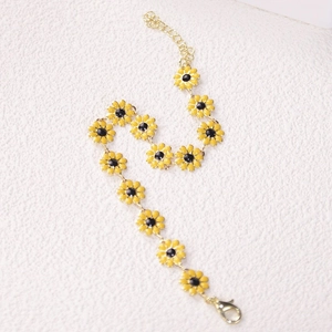 Detail of gold chain bracelet featuring yellow daisy charms with black enamel center
