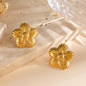 Elegant gold flower stud earrings with textured petals on a minimalist stone background