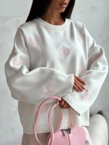 Detail of white knit sweater with pink heart patterns and matching pink leather handbag
