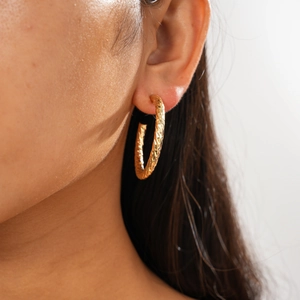 Close-up of a gold geometric C-shaped earring with faceted texture on a model's ear