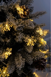 Detail of warm yellow snowflake LED string lights on a snowy Christmas tree branch