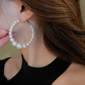 Detailed close-up of a large circular pearl earring worn on the side by a model